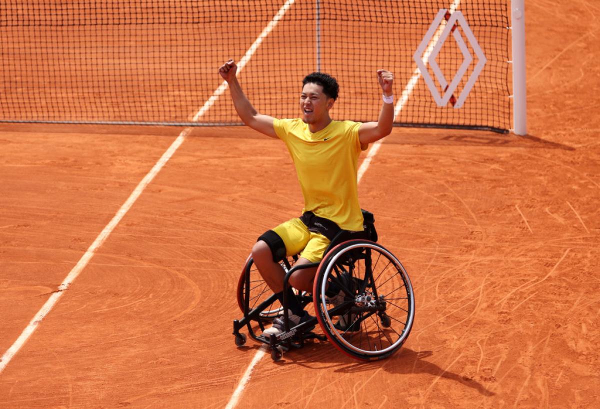 A male wheelchair tennis player celebrates after winning match point on clay court